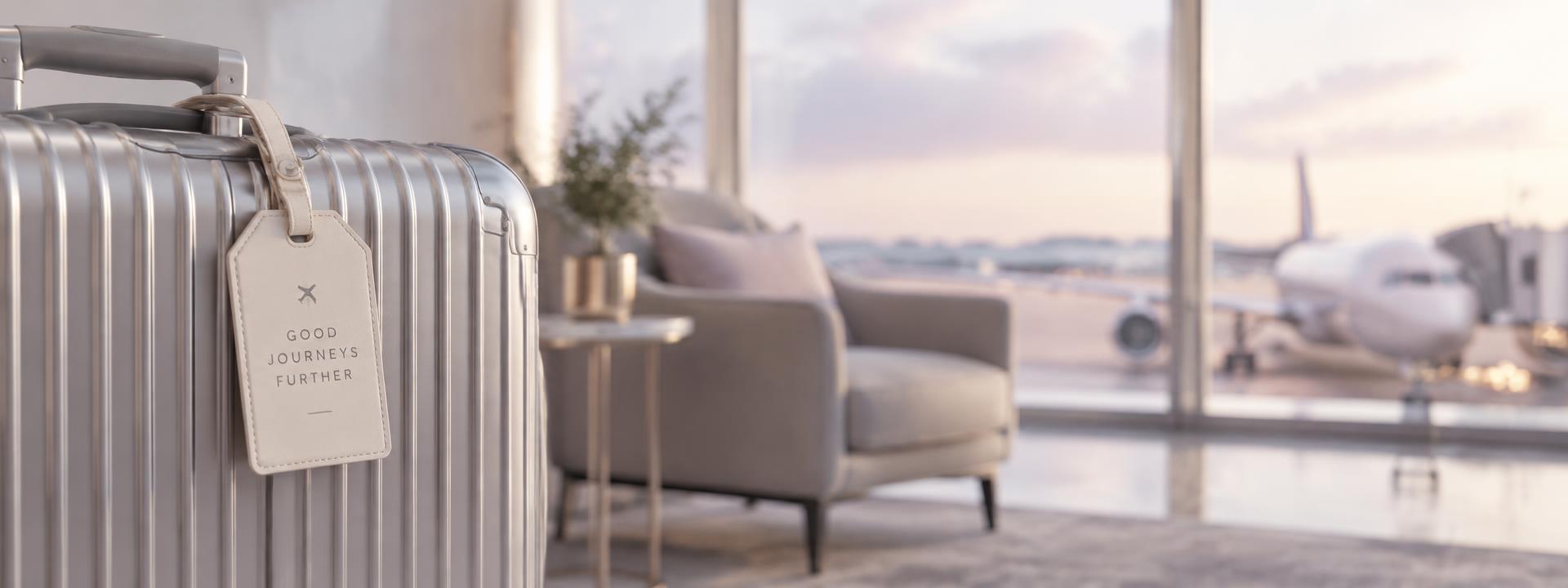 A silver suitcase with a cream luggage tag reading More Journeys Together in an airport lounge